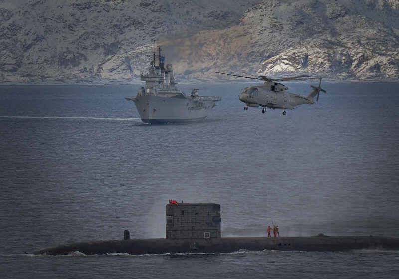 HMS Talent conducts a high line transfer with a Merlin helicopter as HMS Ark Royal passes in the background HMS Talent conducts a high line transfer with a Merlin helicopter as HMS Ark Royal passes in the background