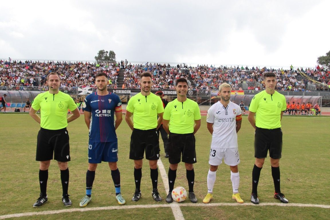 El colegiado madrileño Álvaro Rodríguez Recio -junto al capitán ceutí-, en el AD Ceuta-Algeciras CF de la 22/23